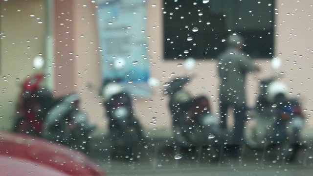 blur raindrops window with old man parking motorbike and walking away
