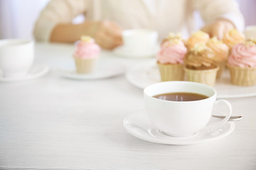 Fototapeta na wymiar Female hands at the table with tea and cupcakes closeup
