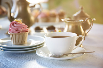 Cupcake with pink cream and cup of tea on wooden table indoors