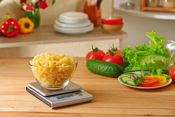 Bowl of dry pasta and digital kitchen scales on wooden table