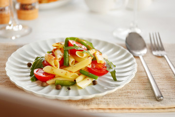 Boiled penne pasta with tomatoes, French bean and arugula on white plate