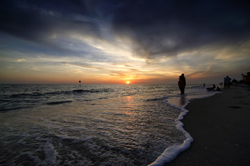 Sunset on the ocean. 
Silhouette of group of people hanging out and enjoy sunset 
