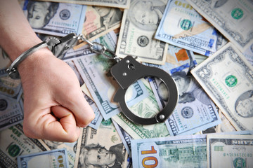 Man in handcuffs clenching fist on dollar banknotes background
