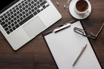 view from above. brown wooden office table with cup of coffee, notepad and laptop computer