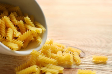 Dry fusilli pasta in white bowl on wooden table