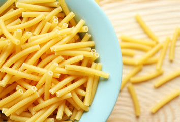 Dry maccheroni pasta in blue plate on wooden table