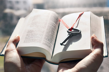 Hands holding a book with vintage key in it. Close up