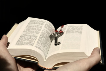 Fototapeta premium Hands holding a book with vintage key on black background.