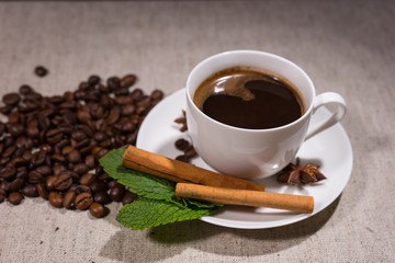 Full cup of coffee with cinnamon sticks and mint