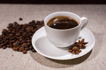 Cup of coffee with spices and beans on tablecloth