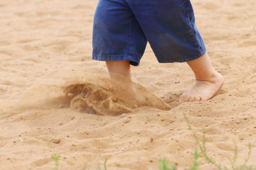 Legs of barefoot of little boy in shorts running on sand