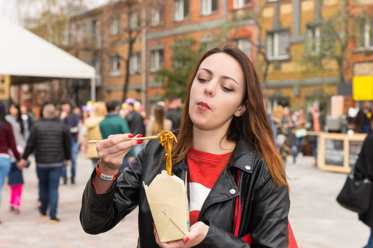 Young Woman Eating Asian Take Out at Busy Festival