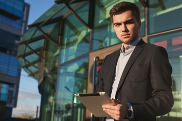 Fototapeta premium Portrait of a man in a suit with a tablet in hands on the background of the building with a glass facade