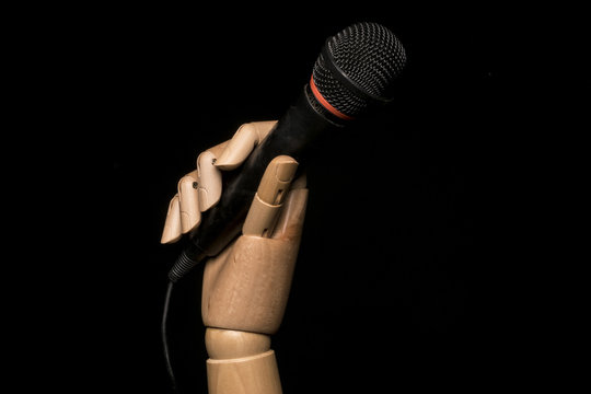 Wooden Hand Holding A Microphone. On Black Background With Copy Space.