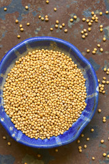 Yellow mustard seeds in small bowl, photographed overhead on slate with natural light (Selective Focus, Focus on the top of the seeds)