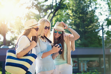 Three attractive girls looking at photos on their camera at summer holidays, girl friends on their travel vacation