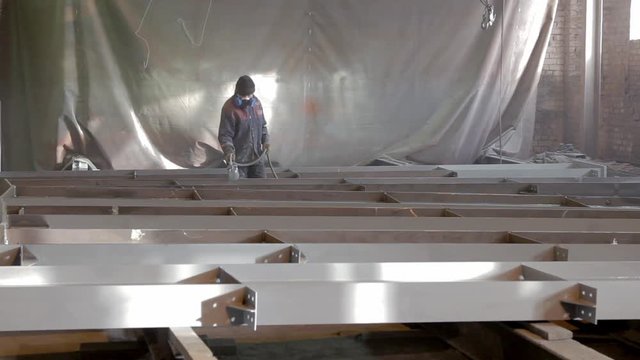 worker is painting a metal beams in a factory