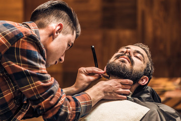 Shaving process of beards in Barbershop. Master makes a haircut beard client with vintage straight razor.