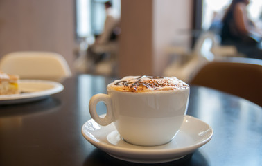 Cup of coffeewith milk foam and cake in cafe