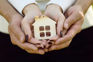 Male and female hand holding a wooden house