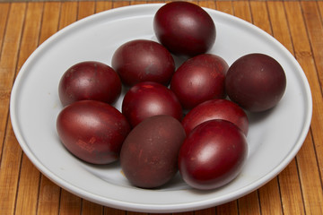 Colorful Easter eggs in a white plate on old wooden table backgr