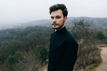 Portrait of handsome catholic bearded man priest or pastor posing outdoors in mountains