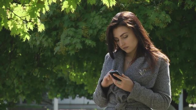 Girl in the park looking at his smartphone. Spring, sunny weather, the background of green leaves