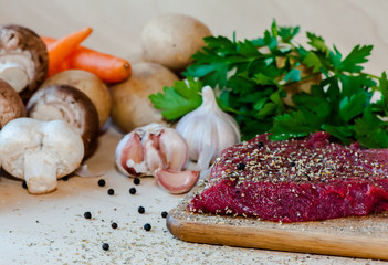 Raw beefsteak with spices and vegetables on wooden background