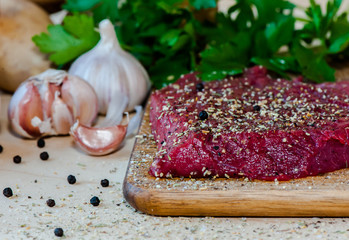 Raw beefsteak with spices and vegetables on wooden background
