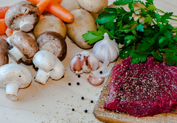 Raw beefsteak with spices and vegetables on wooden background