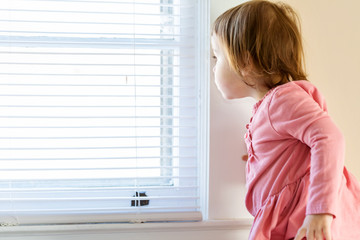 Toddler girl peeking out of the window