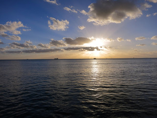 Naklejka premium Sunset streams through the clouds with boats on the water
