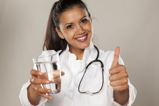 Smiling woman doctor holding a glass of water and showing thumbs up