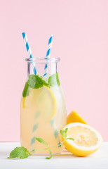 Bottle of homemade lemonade with mint, ice, lemons, paper straws and pastel pink background