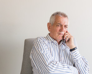 Older man in striped shirt talking on mobile phone and looking concerned