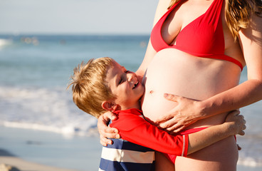 little boy hugging pregnant mother tummy at beach