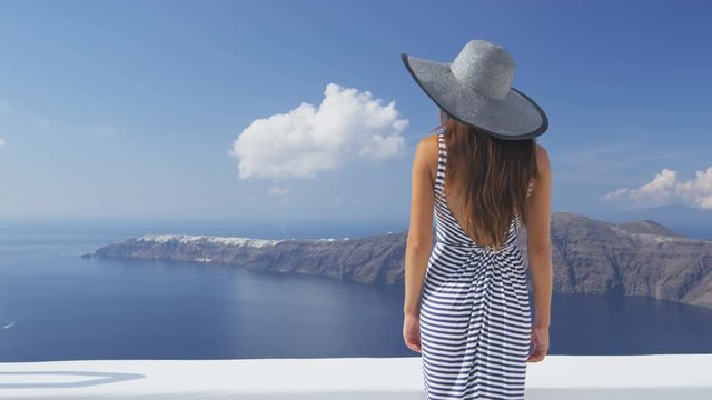 Luxury travel vacation woman looking at view on Santorini famous Europe tourist destination. Elegant young lady living fancy jetset lifestyle wearing dress on holidays. Amazing view of sea and Caldera