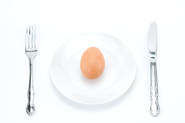 One raw fresh egg on dish  with fork and knife.