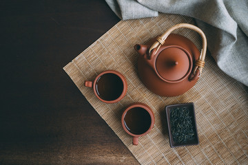 Chinese Tea Ceremony. Brown ceramic teapot and brown tea cup .Green tea on bamboo mat on aged...