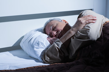 Senior man is sleeping in his bed.