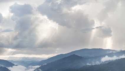 Obraz premium Sun rays light through the clouds in the mountains, dramatic late afternoon scene.
