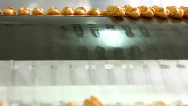 Eclairs slide down conveyor line. Rows of eclairs on conveyor. Confectionery plant machinery. Production of sweet food.