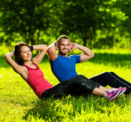 Man and woman exercising at the city park. Beautiful young multiracial couple. Sit ups fitness...