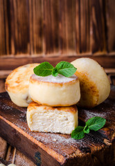 Fritters of cottage cheese with strawberries, sugar powder and mint on wooden background. Selective focus