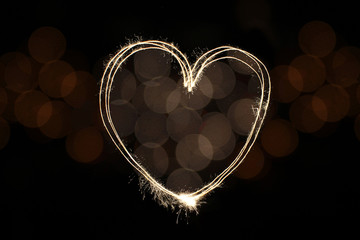 Fire golden sparklers drawn in heart shape overlay on defocused light bokeh for Valentine’s day concept