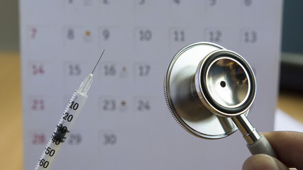 syringe and stethoscope on calendar background
