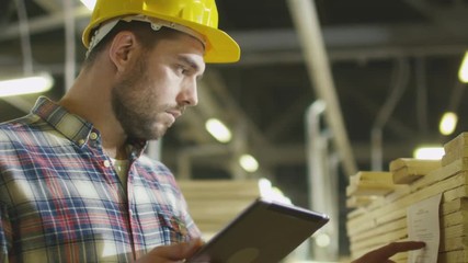 Worker counts wood stock using a tablet computer at a lumber factory warehouse. Shot on RED Cinema Camera. - Powered by Adobe