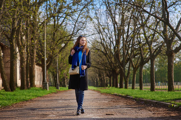 young woman in coat walking at blossoming spring cherry garden