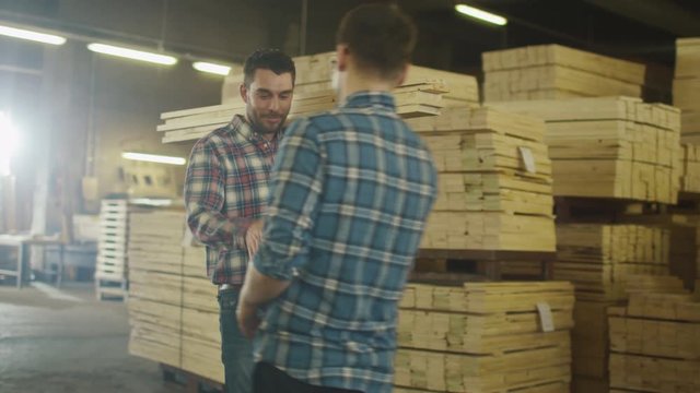 Lumber mill worker in hardhat is carrying wood in warehouse while shaking hand with a coworker. Shot on RED Cinema Camera.