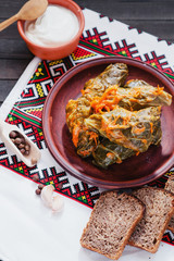 
National traditional Ukrainian and Russian cuisine , a dish called cabbage rolls , stewed rice with minced meat in cabbage leaves with sour cream , carrots and spices on a wooden background